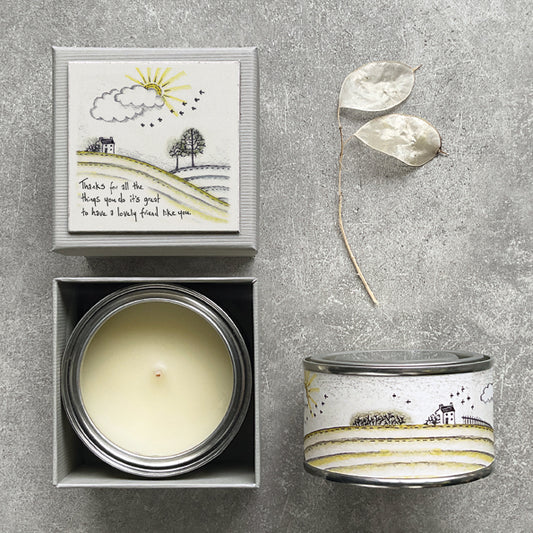 Candle in a box with a decorative lid featuring a landscape design on a gray surface.