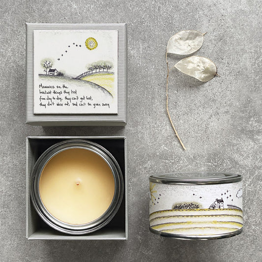 Candle in a box with a decorative lid featuring a landscape design on a gray surface.