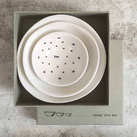 Set of three white ceramic bowls with star patterns and text in a box on a textured surface
