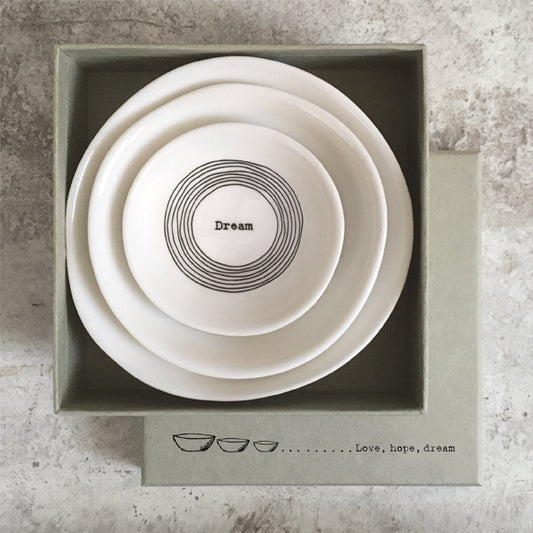 Set of three white bowls with concentric circles and text in a box on a textured surface