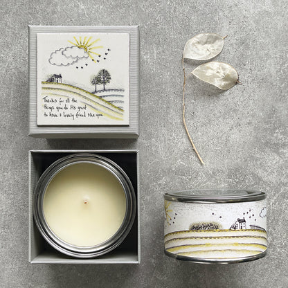 Candle in a box with a decorative lid featuring a landscape design on a gray surface.