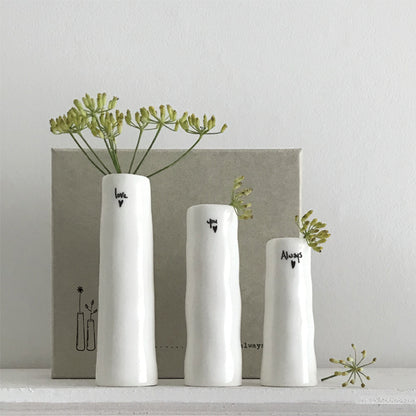 Three white vases with black text and greenery on a light gray background