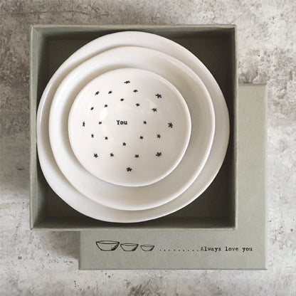 Set of three white ceramic bowls with star patterns and text in a box on a textured surface