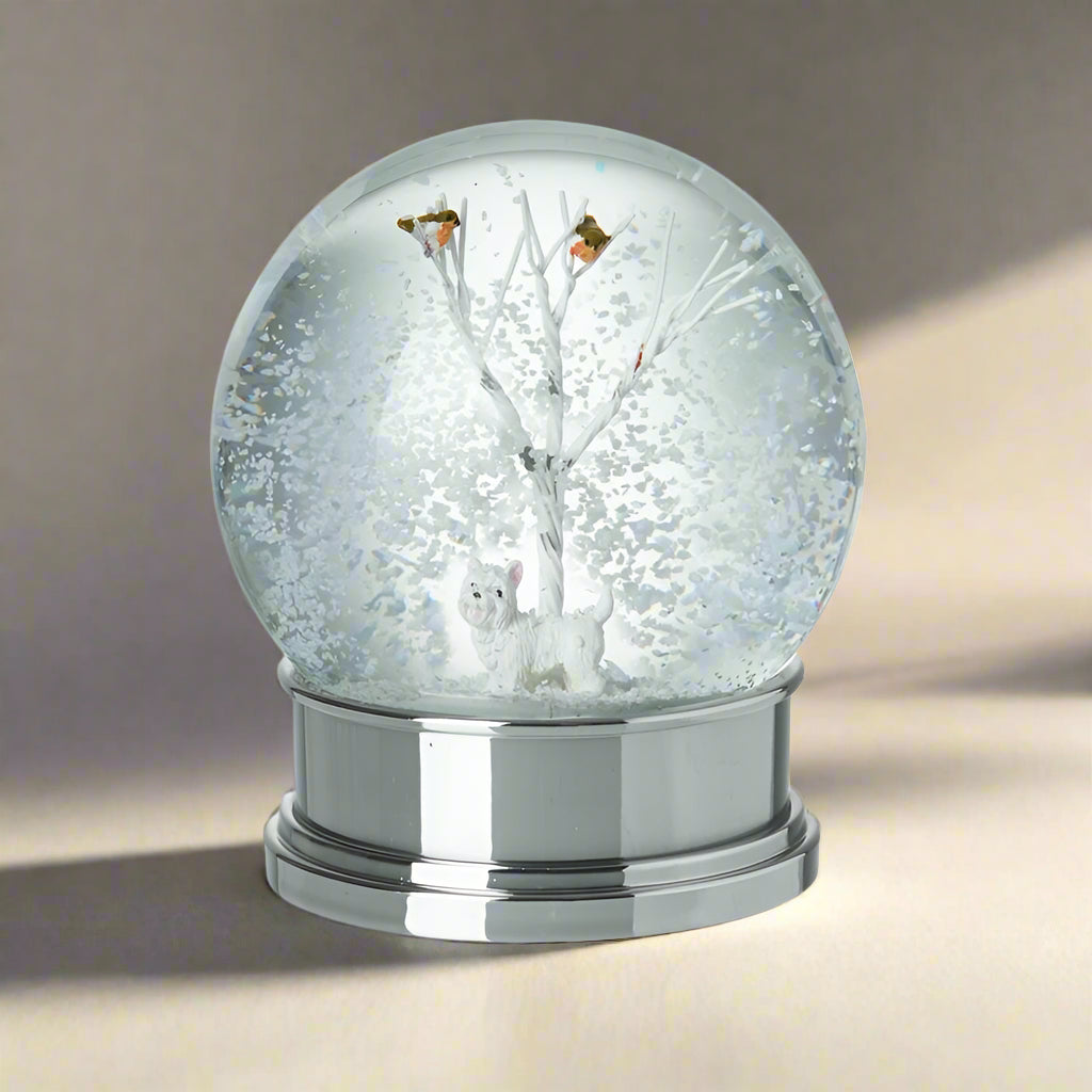 Snow globe with a silver base, featuring a tree and two dogs inside on a white background