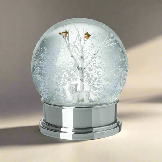 Snow globe with a silver base, featuring a tree and two dogs inside on a white background