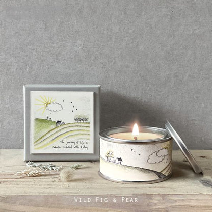 Candle in a tin with a framed illustration on a wooden surface