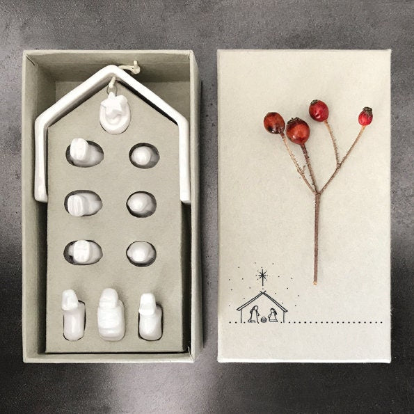 White ceramic nativity set with stable and figures on a gray surface and inside box.