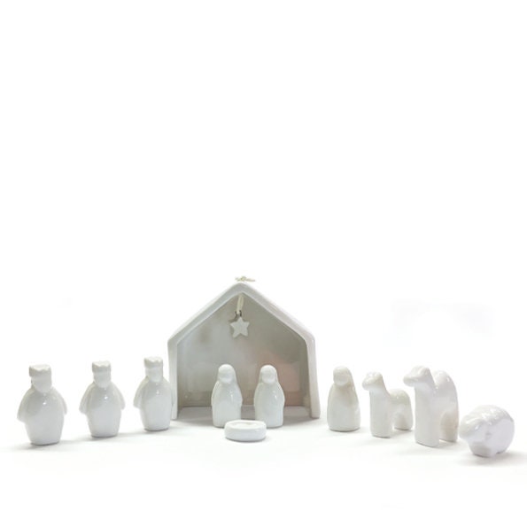 White ceramic nativity set with stable and figures on a white background.