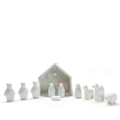White ceramic nativity set with stable and figures on a white background.