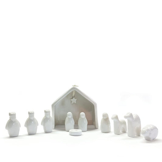 White ceramic nativity set with stable and figures on a white background.