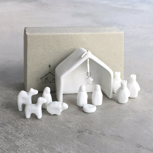 White ceramic nativity set with stable and figures on a gray surface.