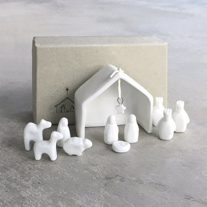 White ceramic nativity set with stable and figures on a gray surface.