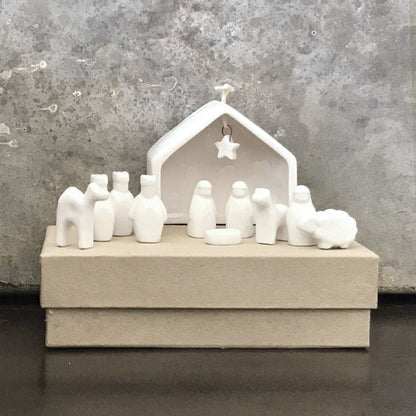 White ceramic nativity set with stable and figures on a gray surface.