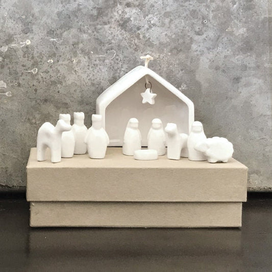 White ceramic nativity set with stable and figures on a gray surface.
