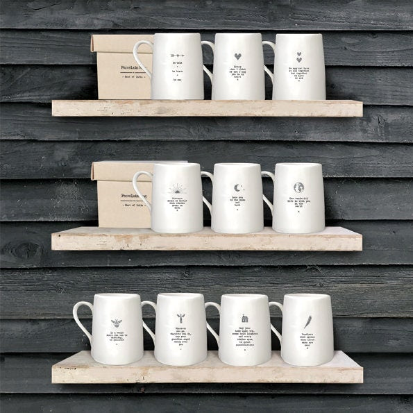 Set of white mugs with text on a wooden shelf against a wooden wall.