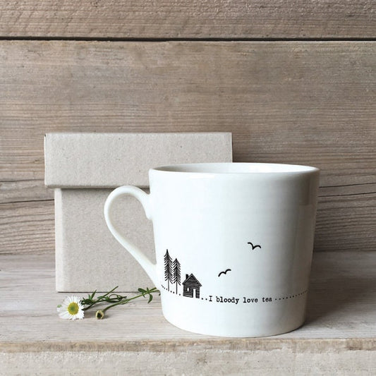 White mug with decorative text and design on a wooden surface with a box and flowers.