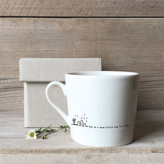 White mug with text on a wooden surface and flower and box