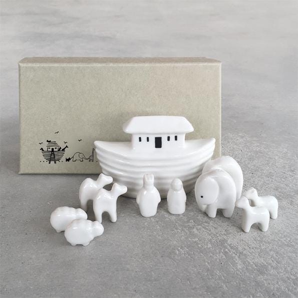 White ceramic Noah's Ark set with animals on a gray surface, featuring a cardboard box in the background.