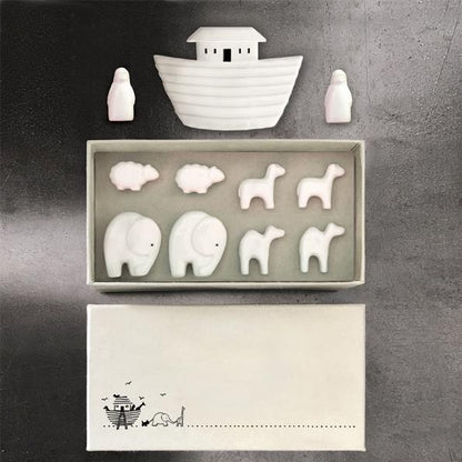 Set of white ceramic animals and a boat in a box on a gray background
