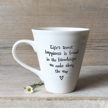White mug with a quote on a wooden surface with a daisy flower.