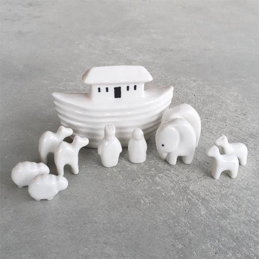 White ceramic Noah's Ark set with animals on a gray surface, featuring a cardboard box in the background.
